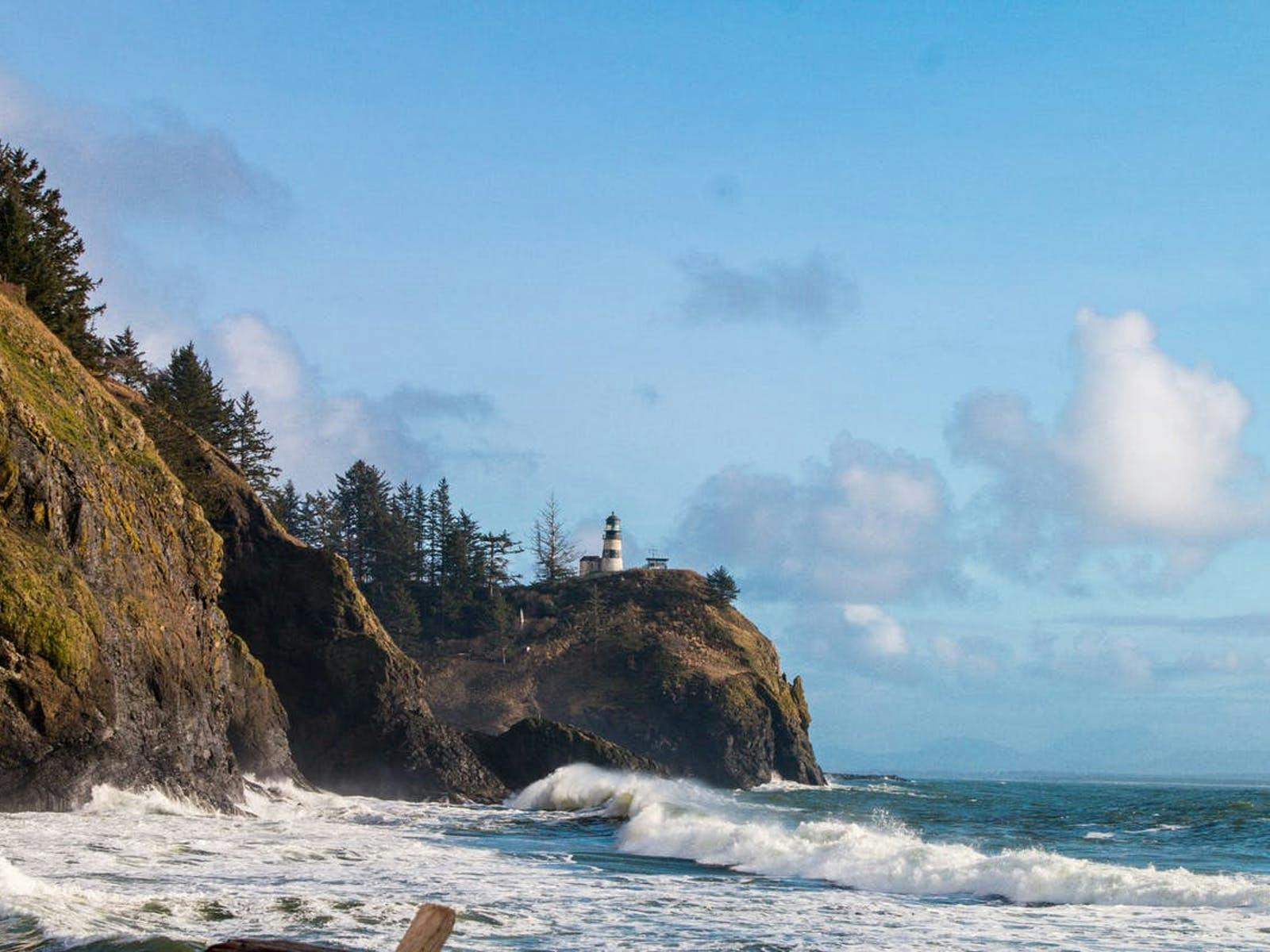 Lighthouse perched above the ocean as waves crash against the Washington coast